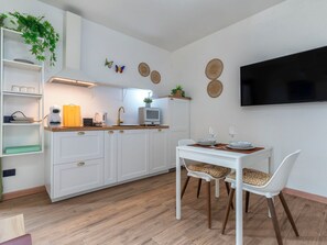 Eine moderne Küche mit weißen Schränken, einem Esstisch mit Stühlen, einem an der Wand montierten Fernseher und dekorativen Wandbildern.