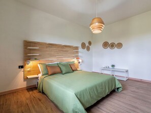 Ein Schlafzimmer mit Bett, Nachttischen, einer Hängelampe, einem Wandregal und einem kleinen weißen Tisch mit Dekoration.