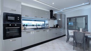 A modern kitchen with built-in appliances, a dining area with wicker chairs, and a large window offering a city view. - Sandra 5 (La Marsa)