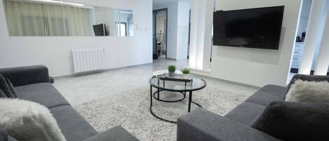 Ett modernt vardagsrum med en grå soffa, ett runt soffbord och en platt-TV som är monterad på väggen.
