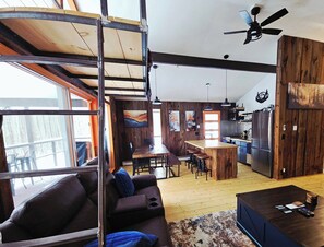 Ein geräumiger Wohnbereich mit hoher Decke, einem Holzespeisetisch, einer Küche mit modernen Geräten und einem großen Fenster, das natürliches Licht hereinlässt.