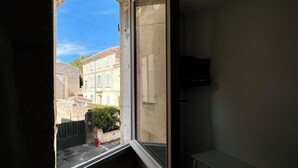 Une fenêtre donnant sur un bâtiment aux murs de pierre, avec une borne d’incendie rouge à l’extérieur.