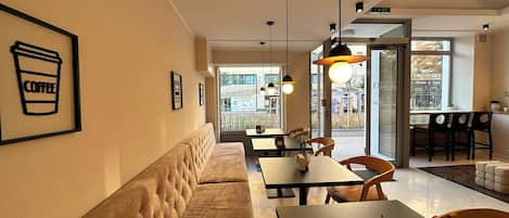 A modern cafe interior with a long cushioned bench, tables, and hanging pendant lights.