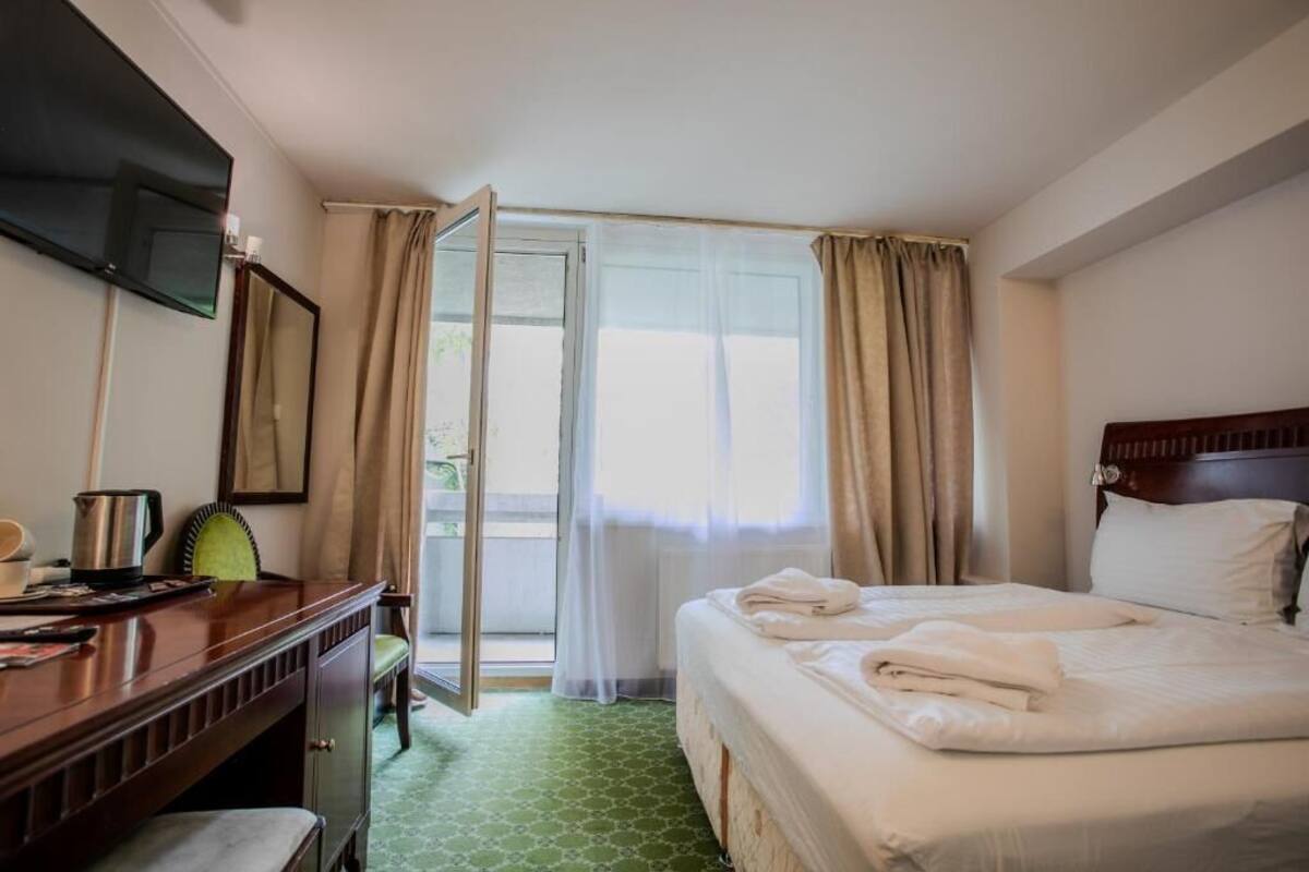 A hotel room with a bed, a desk, a chair, a television, and a window with curtains.