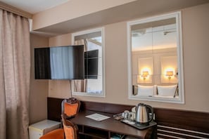 A hotel room with a TV, a desk with a chair, a bedside table with a lamp, and a mirror. - Hotel Attaché (Vienna)
