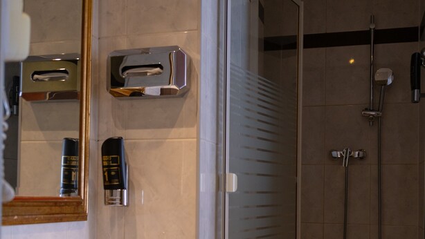 A bathroom with a sink, mirror, towel dispenser, and a glass-enclosed shower area. - Hotel Attaché (Vienna)
