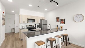 A modern kitchen with a central island, stainless steel appliances, and bar stools. - Exquisite 1BR 30 min to FIFA (Bayonne)
