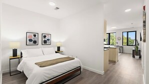 A modern bedroom with a bed, bedside lamps, and artwork on the wall. - Exquisite 1BR 30 min to FIFA (Bayonne)
