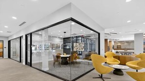 A modern interior with a glass partition, a dining area with yellow chairs, and a visible kitchen area.