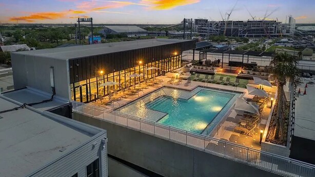 A rooftop pool area with lounge chairs and umbrellas, surrounded by modern buildings.