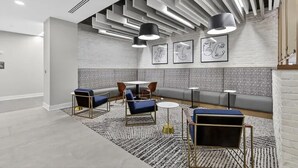 A modern lounge with a high ceiling, geometric light fixtures, a patterned wall, and a seating area with sofas and tables.