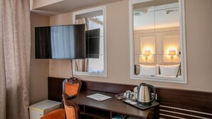 Ein Hotelzimmer mit Fernseher, Schreibtisch mit Stuhl, Nachttisch mit Lampe und Spiegel.