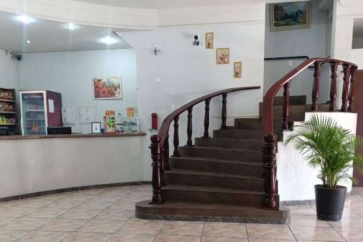 Uma área de recepção com escada de madeira, piso ladrilhado e balcão de atendimento.