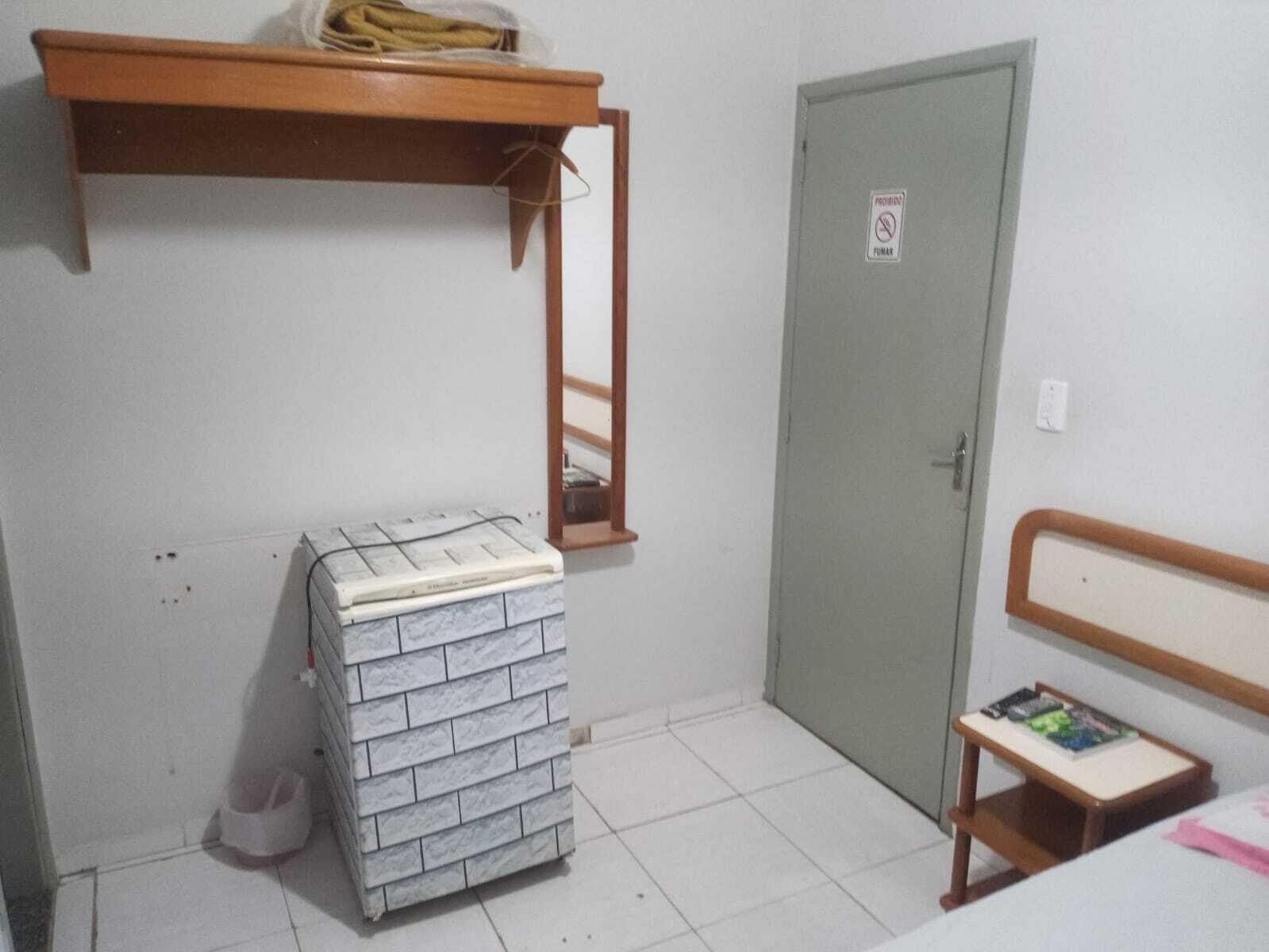 Una habitación pequeña con una cama litera, una estantería de madera, una puerta con un letrero de 'No Fumar' y una mesita de noche.