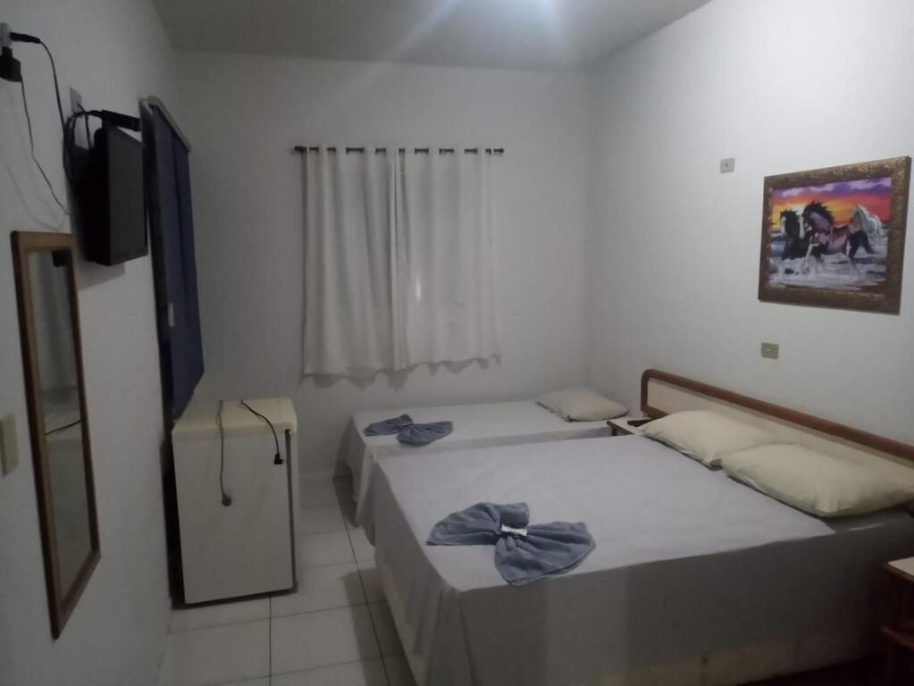 Una habitación con una cama, un pequeño escritorio, un televisor y una ventana con cortinas.