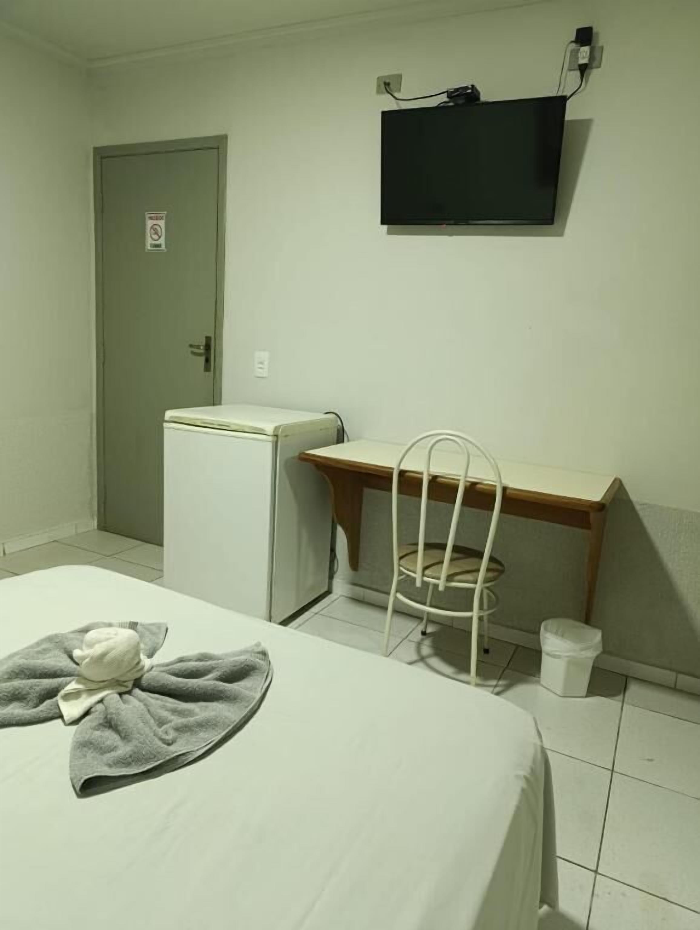 Ein kleines Zimmer mit Bett, Schreibtisch, Stuhl, Fernseher und einer Tür.