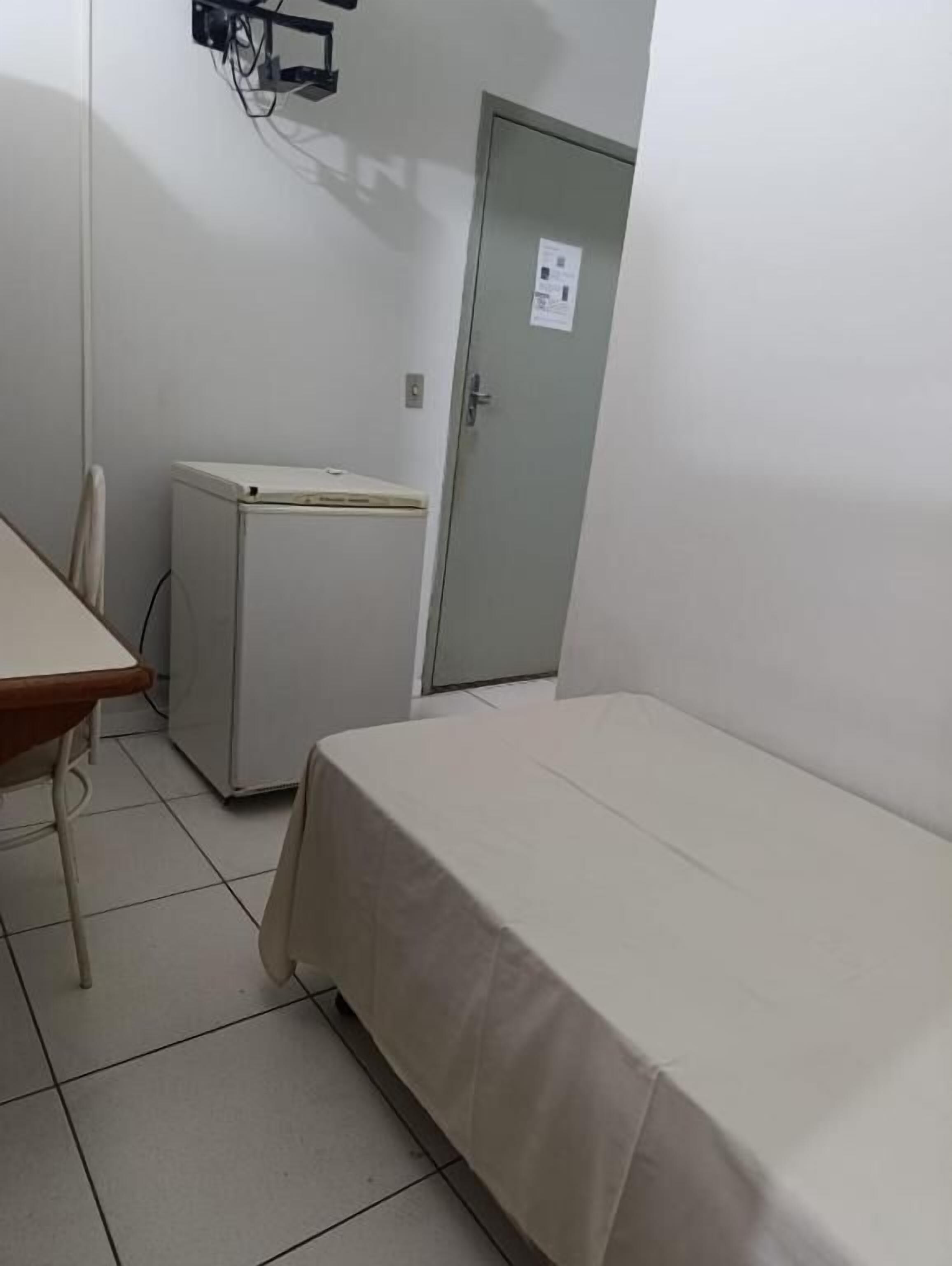 Una habitación pequeña con una cama individual, un escritorio y un refrigerador.