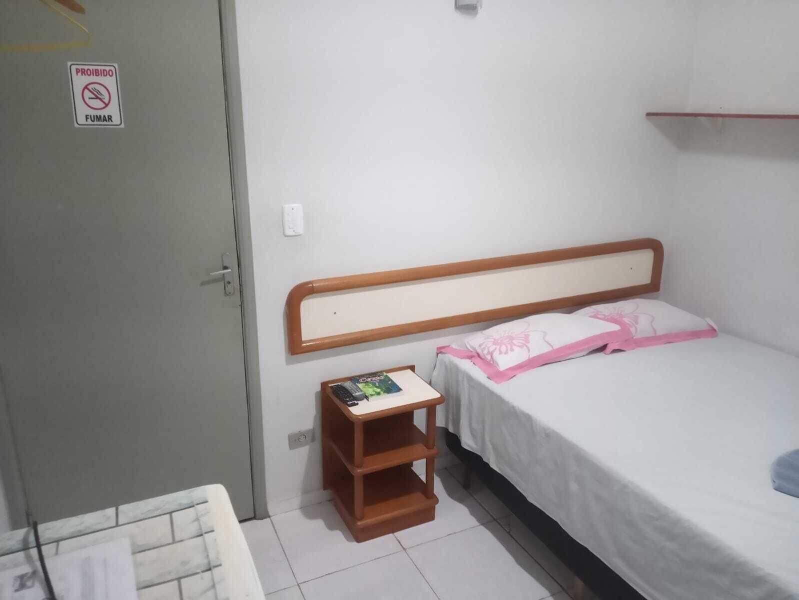A bedroom with a bed, a nightstand, a door, and a 'PROHIBIDO FUMAR' sign.