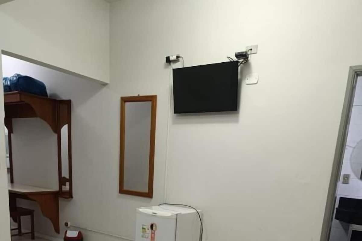 Quarto de hotel com cama, televisão, mini-frigorífico, espelho e porta para um banheiro.