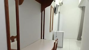 Una habitación pequeña y estrecha con una mesa y sillas de madera, un espejo y un refrigerador blanco.