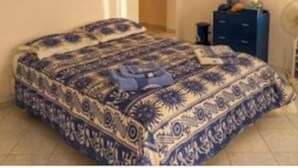 A bedroom with a patterned bedspread, a dresser, and a framed picture on the wall.
