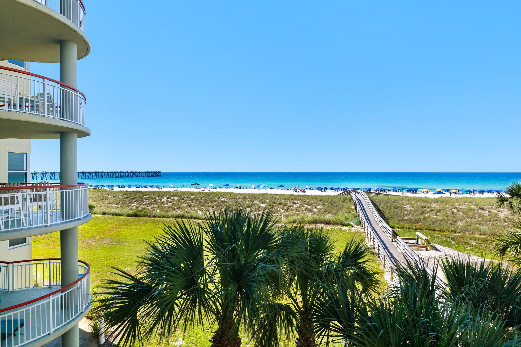 A beachfront hotel with a view of the ocean, a pier, and palm trees.