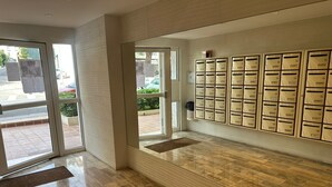 Un vestíbulo con puerta de vidrio, buzón empotrado en la pared y suelo de madera pulida.