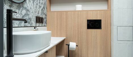 A modern bathroom with a wooden vanity, a sink, a toilet, and a shower area.