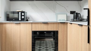 A modern kitchen with dark cabinets, a microwave, a stove, and a built-in oven. - RentPlanet - Apartament Wałowa (Warsaw)