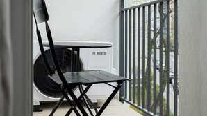 A balcony with a Bosch air conditioning unit, a foldable chair, and a metal railing. - RentPlanet - Apartament Wałowa (Warsaw)