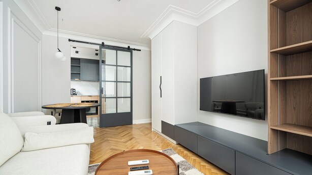 A modern living room with a sofa, a coffee table, a TV, and a sliding door leading to a kitchen. - RentPlanet - Apartament Wałowa (Warsaw)