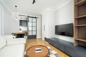 Ein modernes Wohnzimmer mit einer Couch, einem Couchtisch, einem Fernseher und einer Schiebetür, die zum Küchenbereich führt.