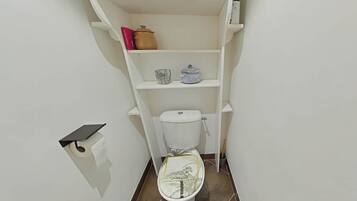 A small bathroom with a toilet, a shelf with a pot and a container, and a roll of toilet paper.