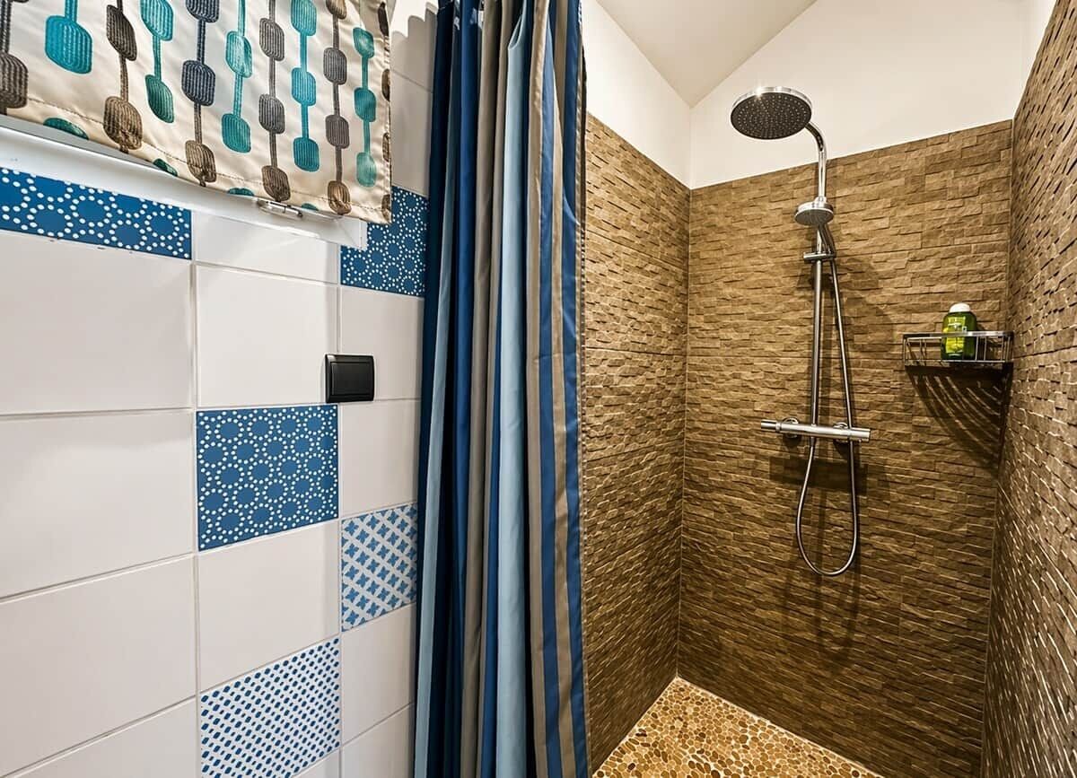 Ducha con cabezal de ducha manual, pared con azulejos de diseño azul y blanco, y repisa con artículos de aseo.