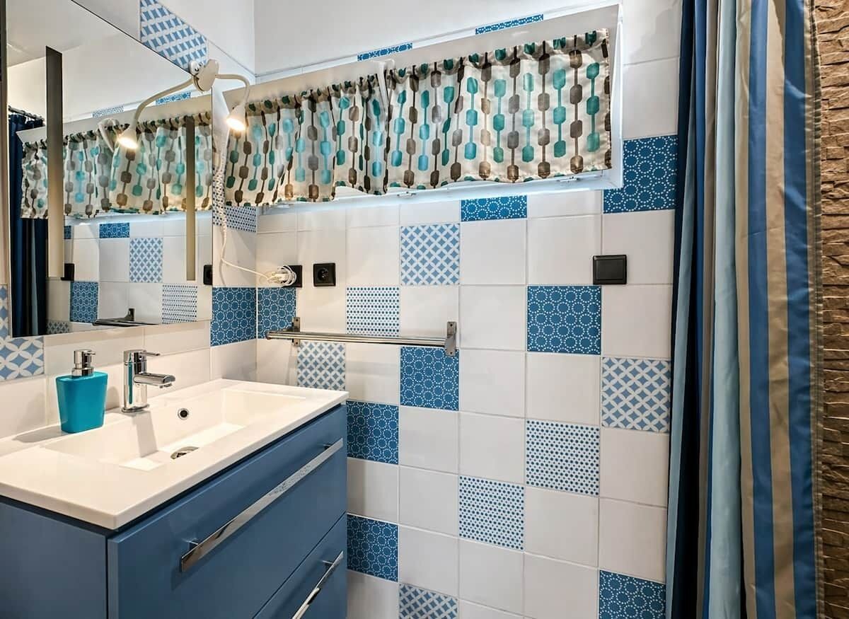 A bathroom with a white sink, blue cabinet, and patterned tiles.