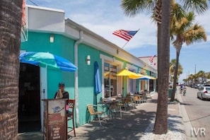 A street with outdoor seating, palm trees, and a storefront with an American flag. - Free Tybee Parking! Private Pool, Fire Pit, Grill (Savannah)