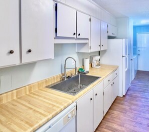 A kitchen with white cabinets, a stainless steel sink, a wooden countertop, and a built-in dishwasher.