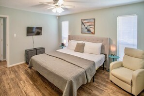 A bedroom with a bed, a chair, a TV, a ceiling fan, and a painting on the wall. - Free Tybee Parking! Private Pool, Fire Pit, Grill (Savannah)