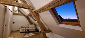 Ein Schlafzimmer im Loft-Stil mit schrägem Dach, integriertem Fenster, einer Couch und einem kleinen Tisch.