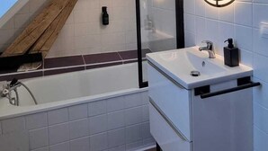 Une salle de bain moderne avec un plafond en pente, une baignoire, un meuble-lavabo avec un miroir et des poutres en bois.