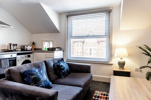 A living room with a grey sofa, a wooden coffee table, a lamp, and a window with blinds. - Fairhaven View by Guestz (Lytham-St-Annes)