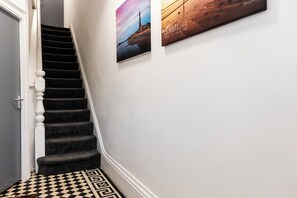 A staircase with a checkered floor leading to a door, a wall with a framed picture, and a wooden panel with text. - Fairhaven View by Guestz (Lytham-St-Annes)