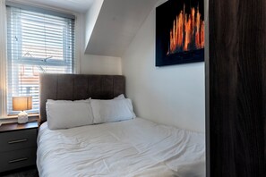 A bedroom with a bed, a nightstand, a lamp, and a painting on the wall. - Fairhaven View by Guestz (Lytham-St-Annes)