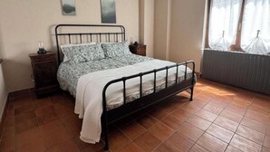 A bedroom with a metal bed frame, a bedside table, a radiator, and a window with curtains.