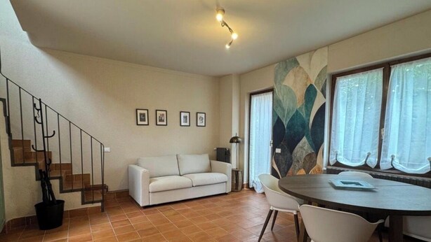 A living room with a sofa, dining table, chairs, a staircase, and a large window with curtains.