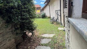 A stone wall, a grassy area with stepping stones, and a building with a door and window.