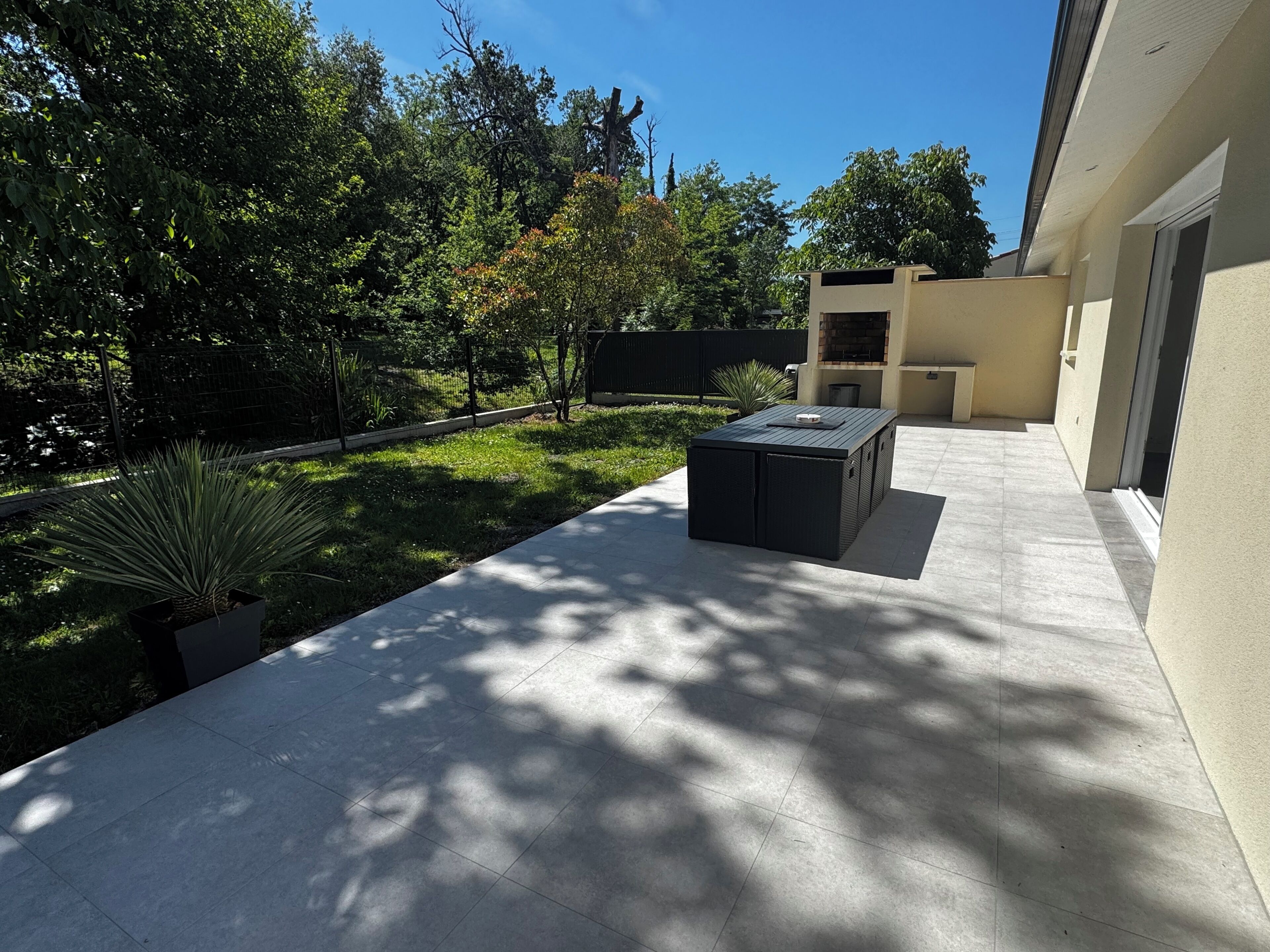 Eine moderne Außenpatio mit integriertem Tisch und Barbereich, umgeben von gepflegtem Rasen und Bäumen.