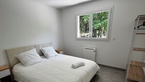 A bedroom with a bed, a window, a radiator, and a wooden shelf.