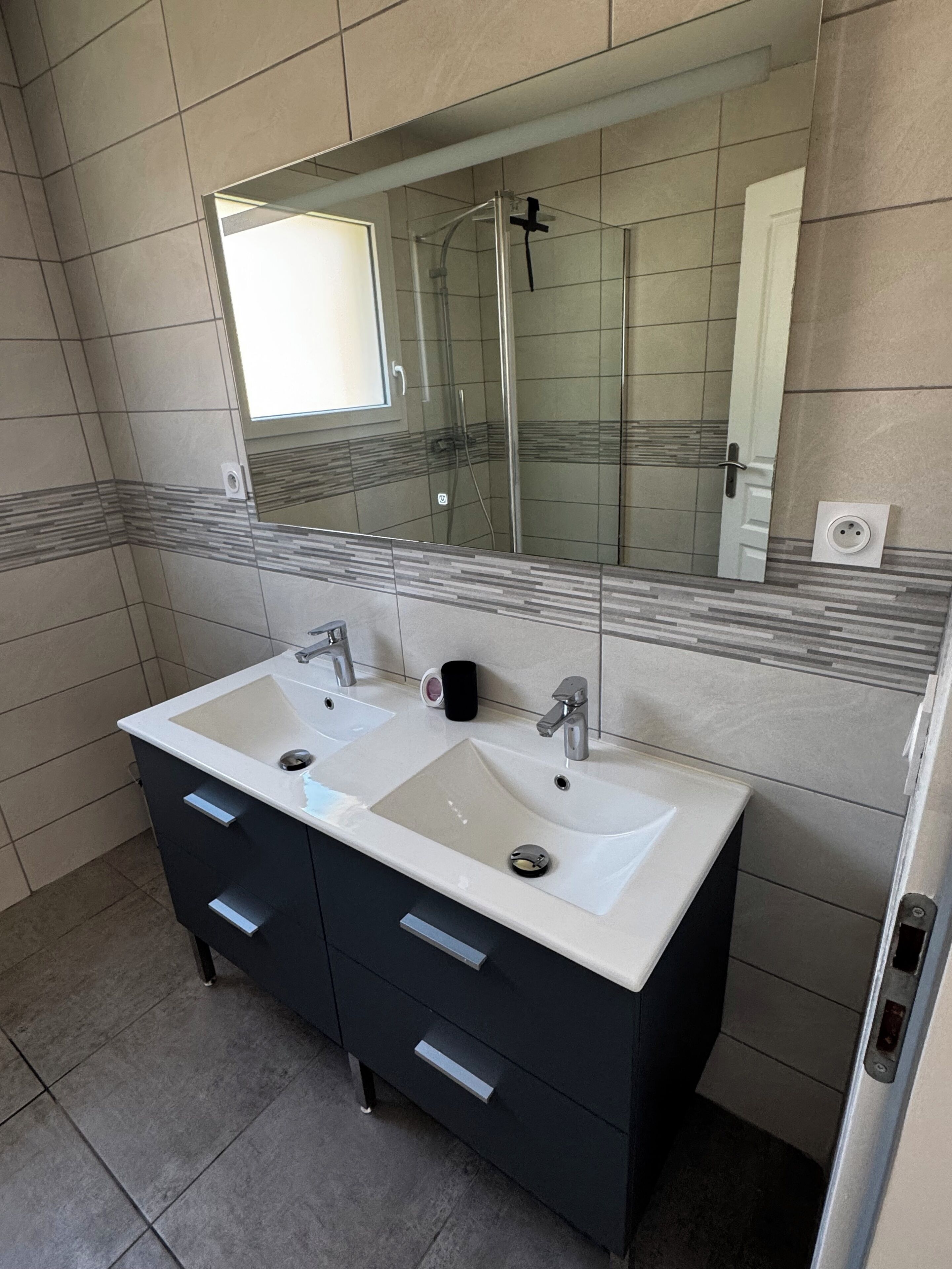 Een badkamer met een wastafelmeubel met dubbele wastafel, een grote spiegel en een douche.