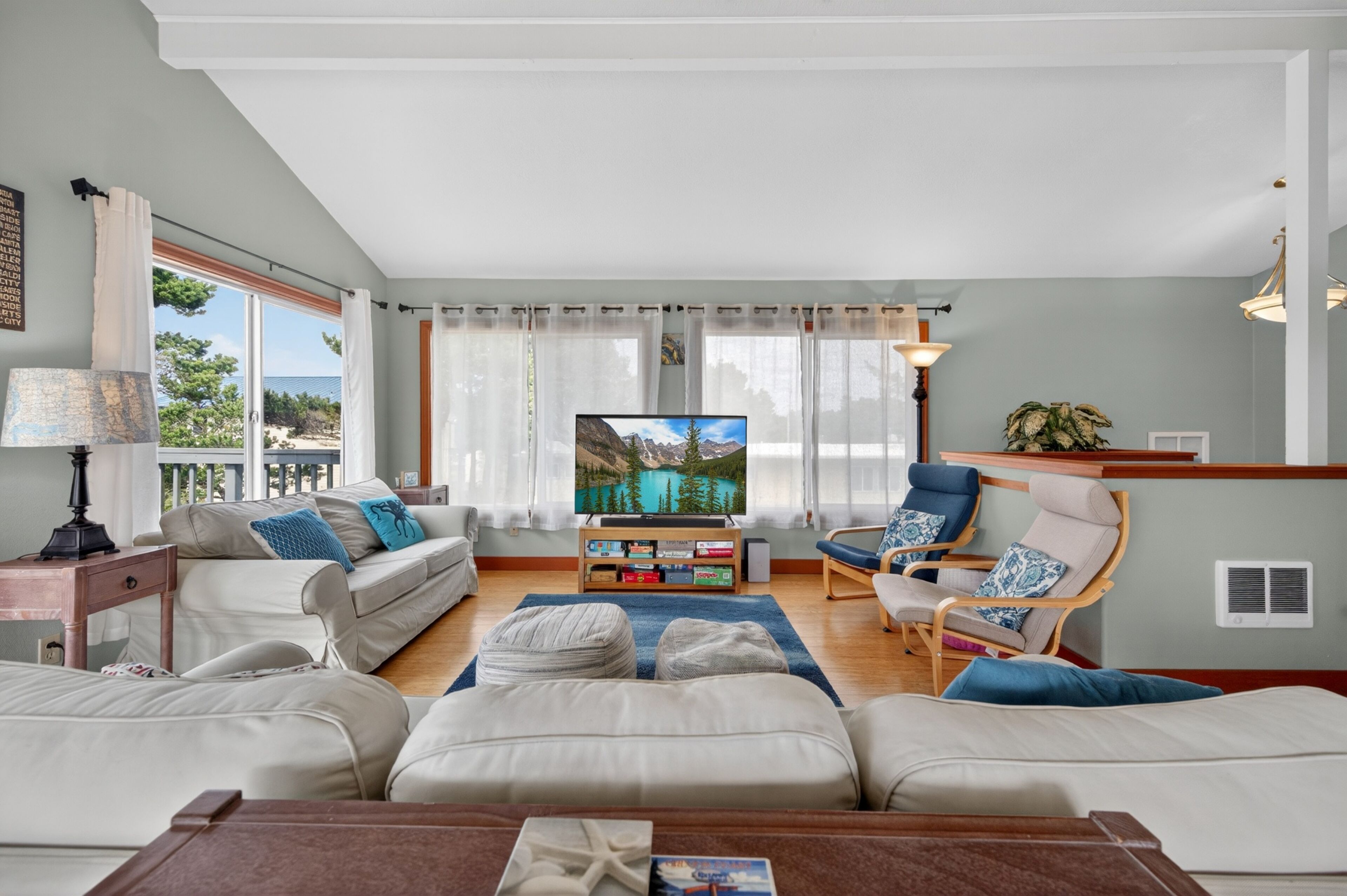 A living room with a sofa, armchairs, a coffee table, a TV, and a view of the outdoors.
